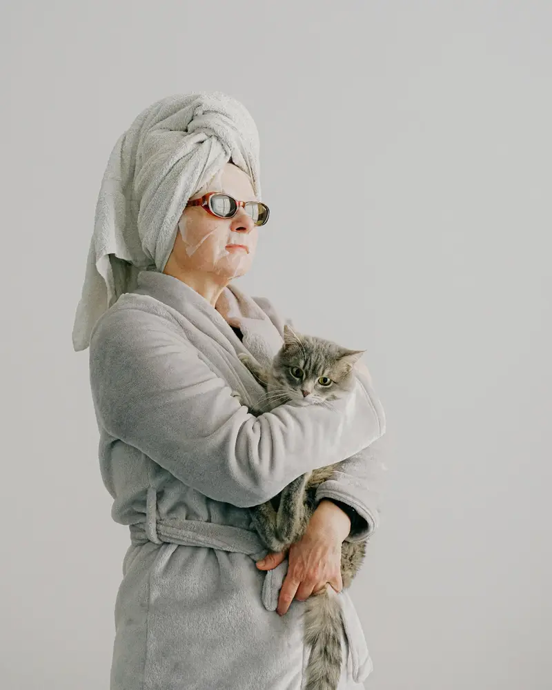 Person wearing a bathrobe and face cream while holding a cat during a self-care moment